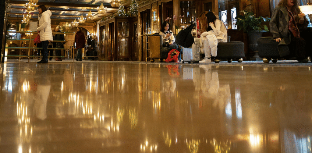 Busy hotel lobby with travelers sitting on luggage, warm lighting reflecting on polished floor