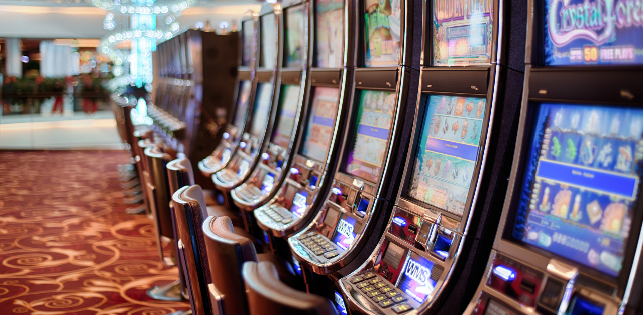 Row of illuminated slot machines in a casino, with colorful screens and patterned carpet creating a vibrant gaming atmosphere