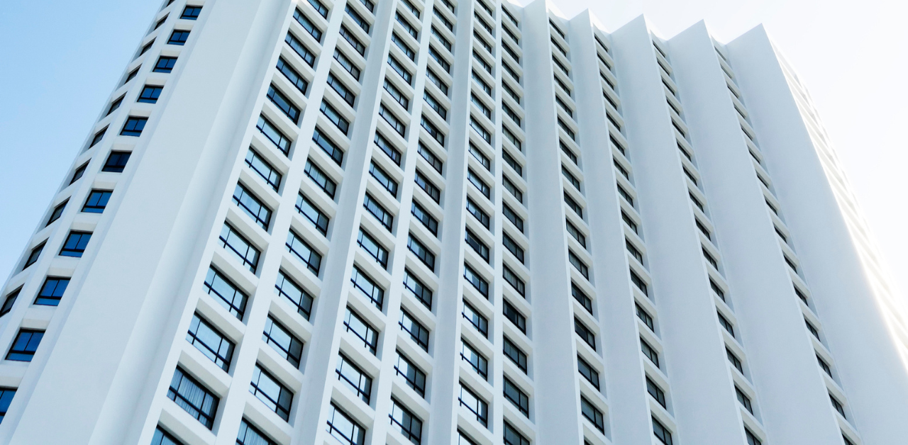 Tall modern high-rise building with repeating windows viewed from below against a clear blue sky