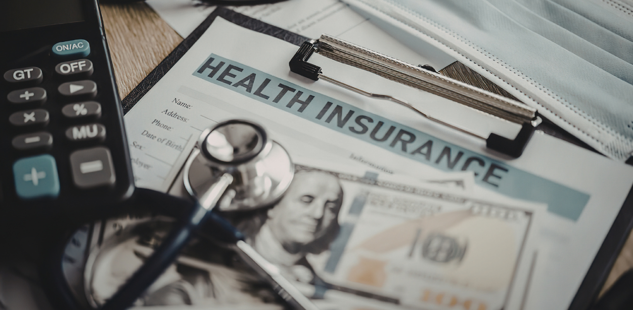 Health insurance paperwork with a stethoscope, calculator, medical mask, and cash spread across a desk