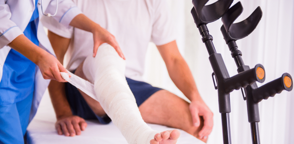 Medical professional wrapping a bandaged leg cast on a seated patient with crutches positioned nearby