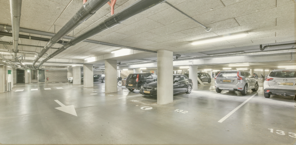 Wide view of an underground parking garage with parked cars, concrete pillars, and directional floor markings