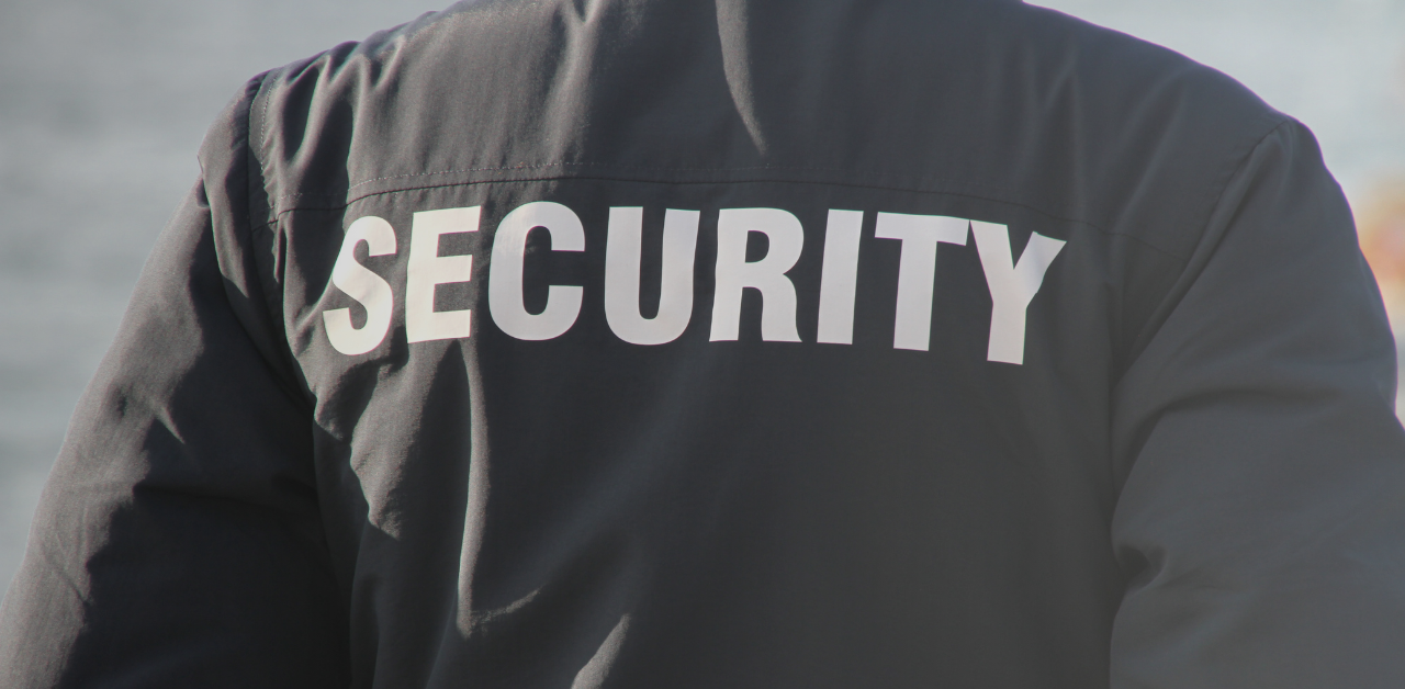Close-up view of the back of a person wearing a black jacket with the word “SECURITY” printed in large white letters