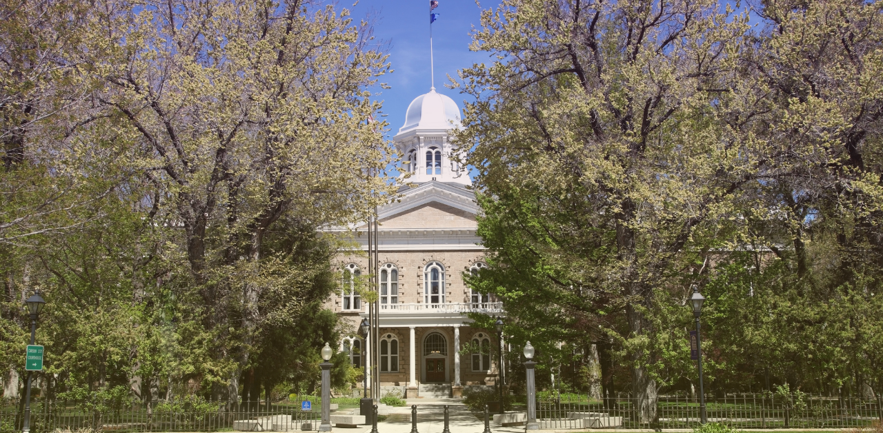 Historic courthouse with a white dome stands behind leafy trees under a clear blue sky