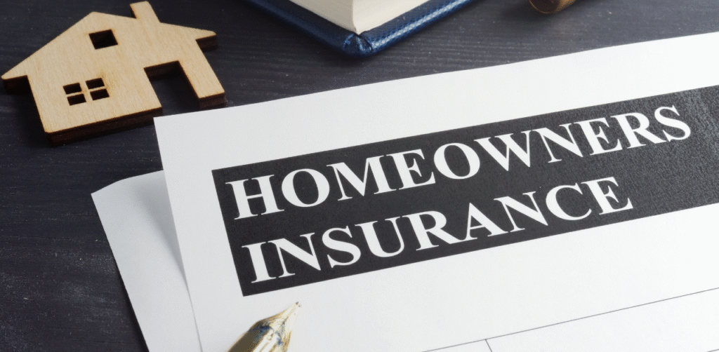 Homeowners insurance paperwork on a desk with a house model, notebook, and pen