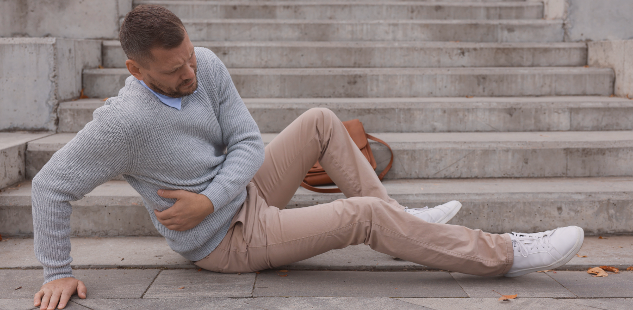 Person sits on concrete steps holding their side, appearing to be in pain after a fall