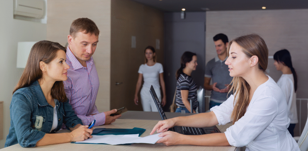 Reception staff assist a couple with paperwork at a service counter in a busy office