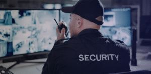 Security guard monitoring multiple surveillance screens while speaking into a handheld radio in a control room