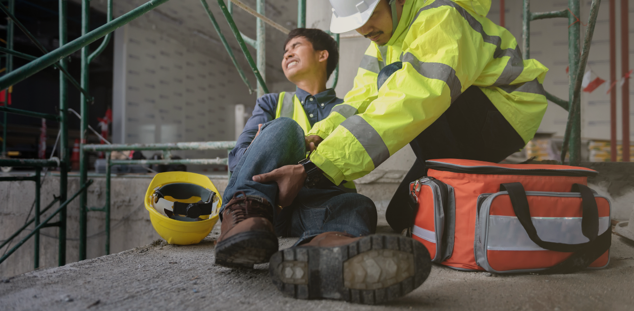 Worker in safety gear assists an injured coworker seated at a construction site