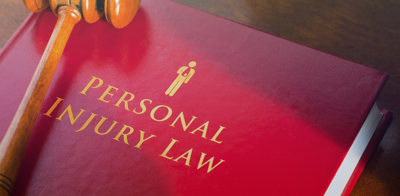 Red law book titled “Personal Injury Law” beside a judge’s gavel on a wooden surface