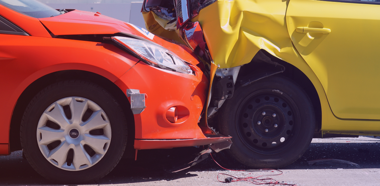 Close-up of a severe collision between a red car and a yellow car, with crumpled body panels, broken trim, and debris scattered on the road