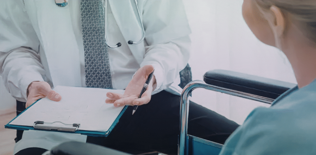 Doctor consults with a seated patient, holding a clipboard and explaining medical information