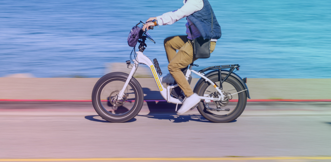 Person riding a compact electric bicycle along a waterfront path, with motion blur emphasizing speed