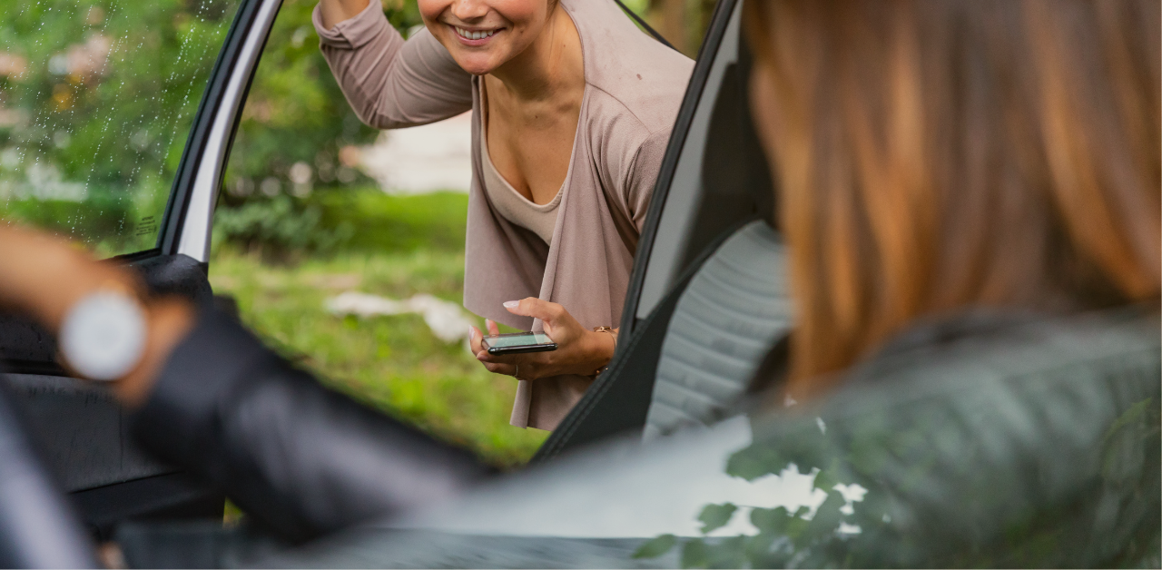 Person standing outside a car smiles while speaking with the driver through the open door