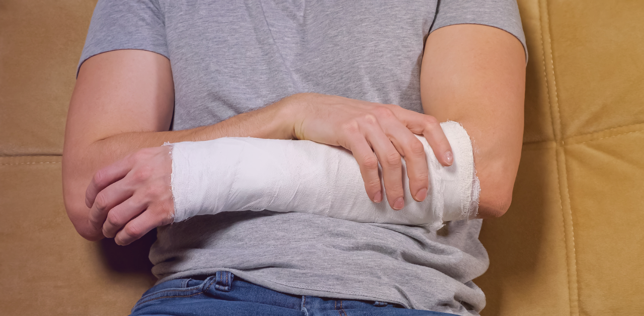 Person with a forearm cast supports the injured arm while seated on a couch