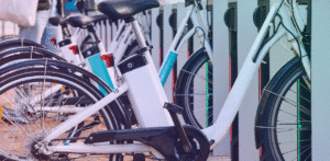 Row of white electric bicycles parked in docking stations, shown in a close-up of their frames, wheels, and charging area