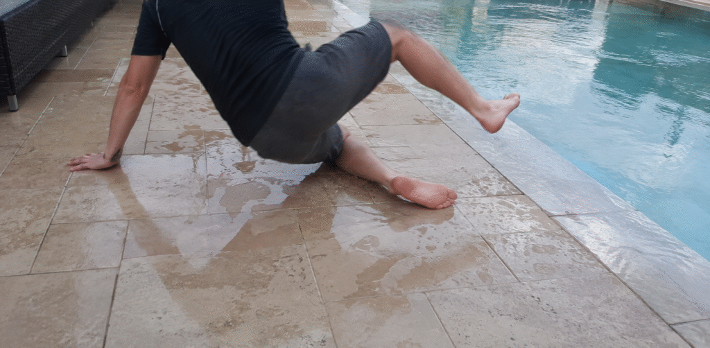 A barefoot person slips and falls on wet tile beside a swimming pool